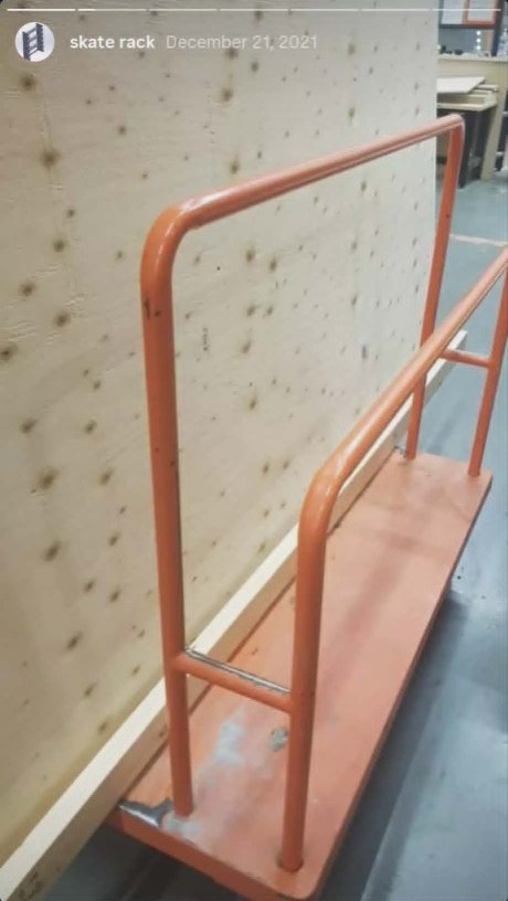 Orange tubular metal rack frame in a workshop — welded uprights and cross members before the plywood build